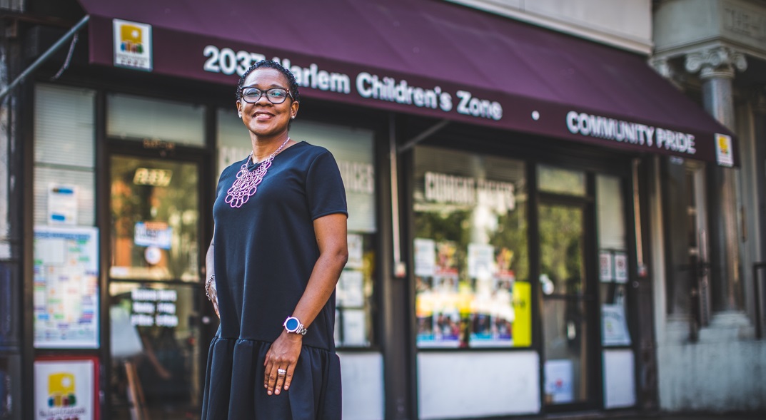 Latasha Morgan, Director of Parent and Community Engagement at Harlem Children's Zone, stands smiling in front of Harlem Children's Zone Community Pride building