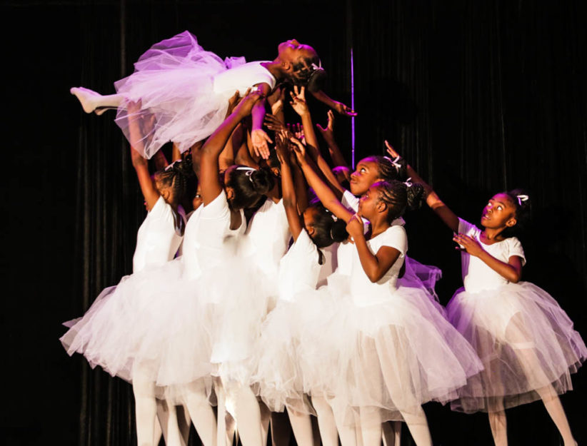 geoffrey canada community center | A group of young ballet dancers lift and hold up one of their fellow dancers on a performance stage.