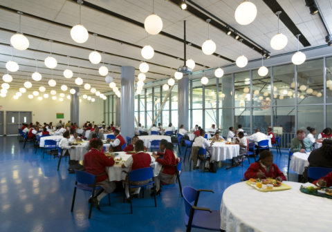 Students and teachers sit at round tables in an event hall eating lunch