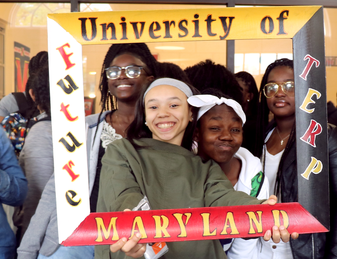 Teen girls smile and hold up a “University of Maryland” decorative frame.
