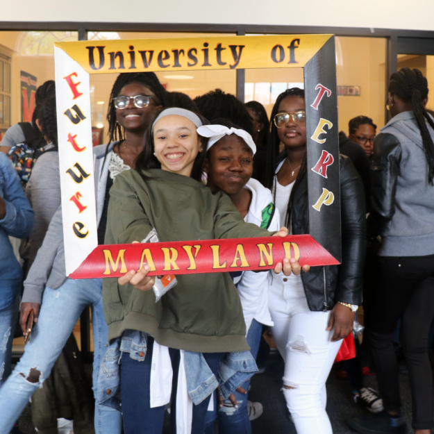 Teen girls smile and hold up a “University of Maryland” decorative frame.