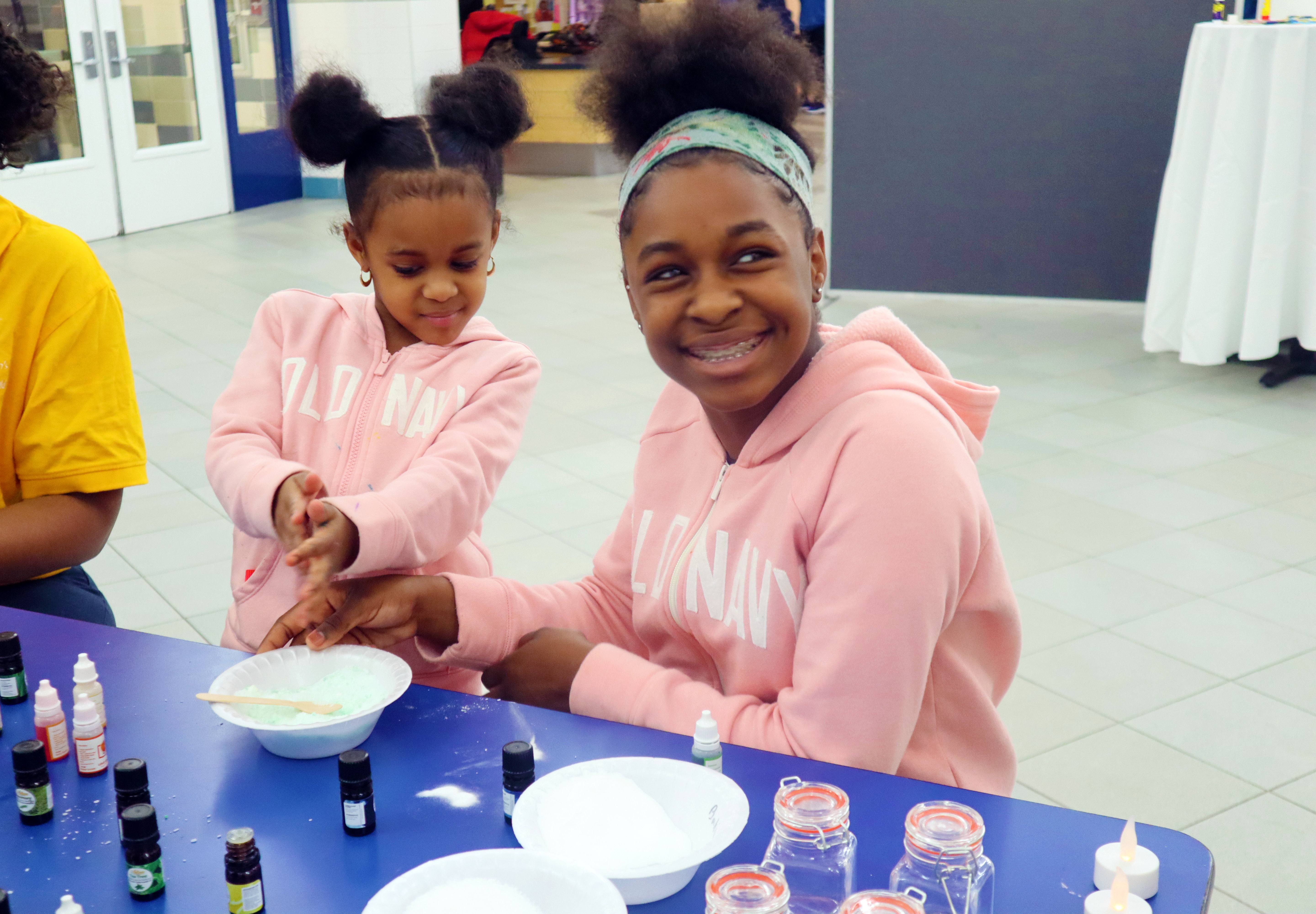 Two girls smiling at a craft table and making bath salts