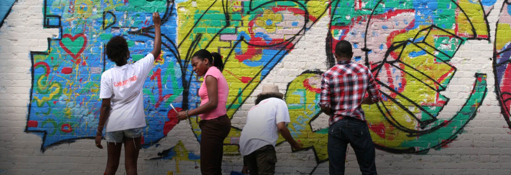 Four volunteers paint a colorful mural on a wall in their community.