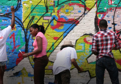 Four volunteers paint a colorful mural on a wall in their community.