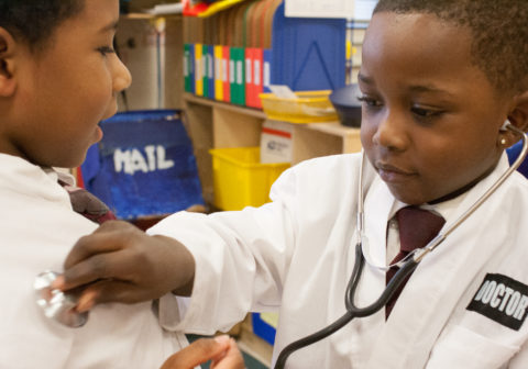 Healthy Harlem | A little boy dressed as a doctor playfully holds a stethoscope to another boy.
