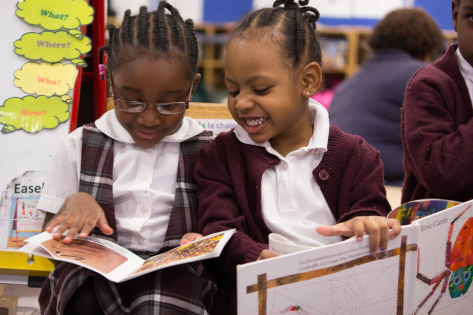 Two preschool students site side by side, smiling and reading together