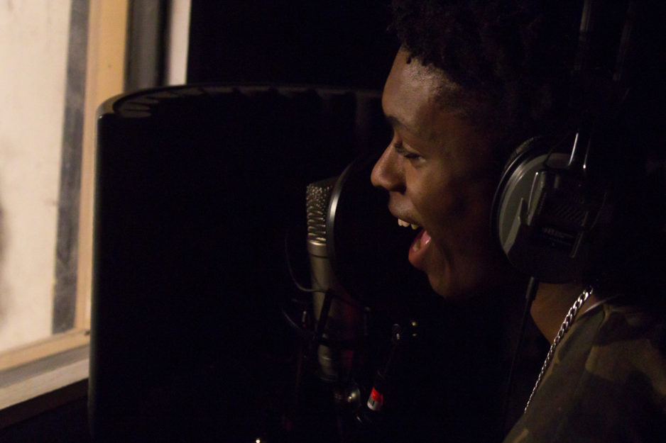 A teen boy sings into a microphone in a recording booth.