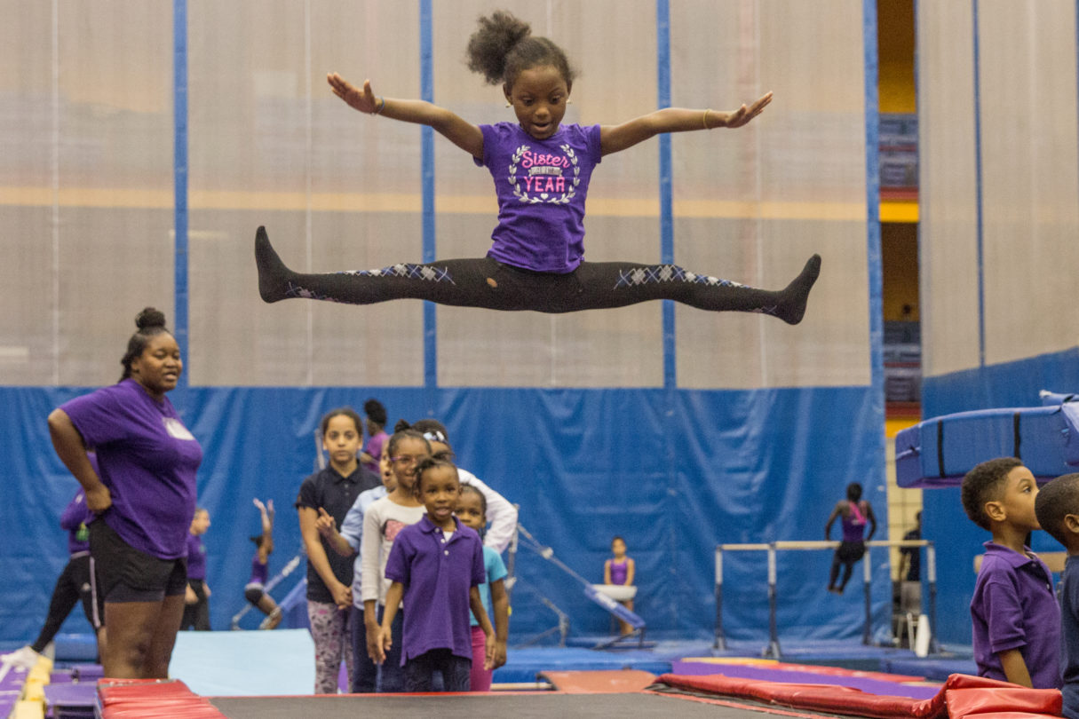 A girl is practicing gymnastics. She is in a mid-air split on a trampoline.