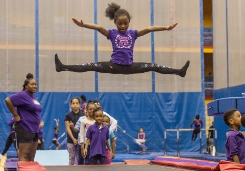A girl is practicing gymnastics. She is in a mid-air split on a trampoline.