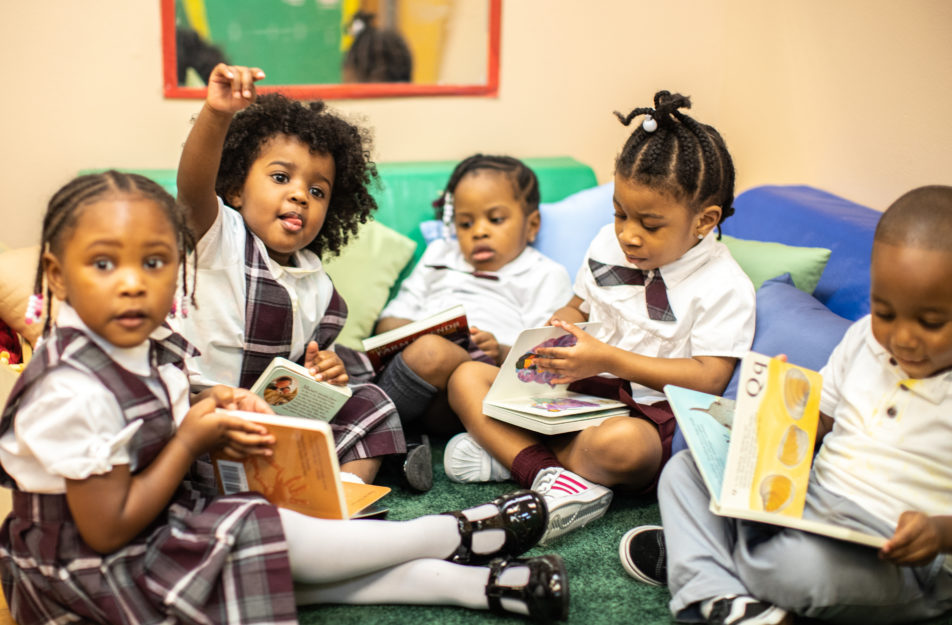 Five preschool students sit in a circle, flipping books, and practicing learning to read