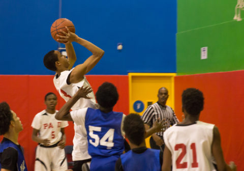 Basketball players surround a player as he takes a jump shot at the hoop