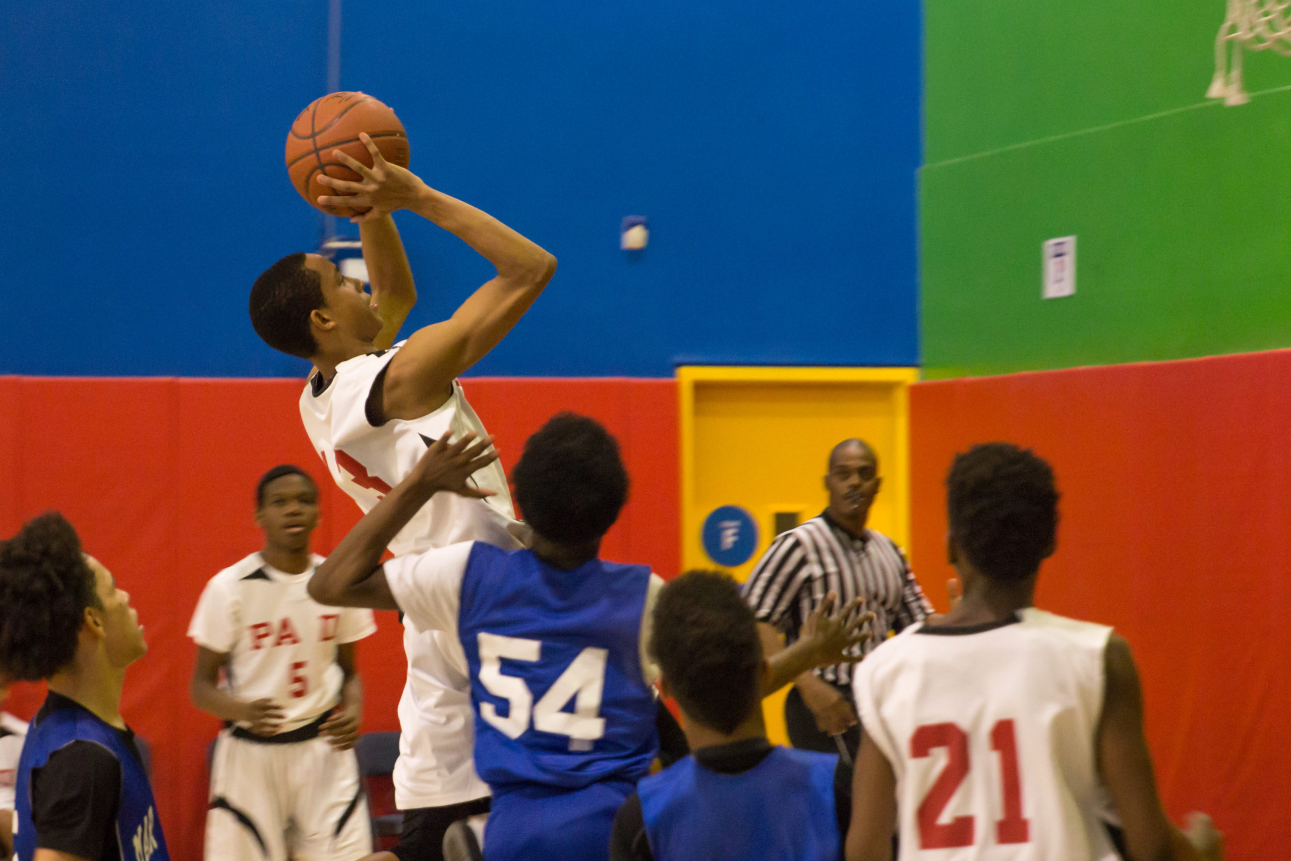 Basketball players surround a player as he takes a jump shot at the hoop