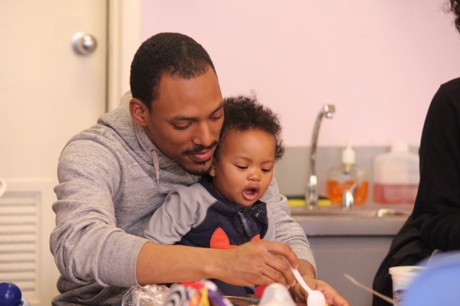 Fathers | With his toddler son sitting on his lap, a father and son do arts and crafts in a classroom