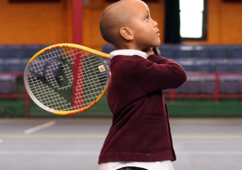 A little boy poses with a tennis racket
