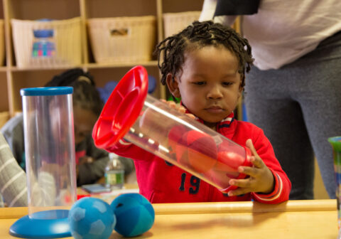 Three-Year-Old journey scholar wearing a red sweatshirt plays with a red ball.