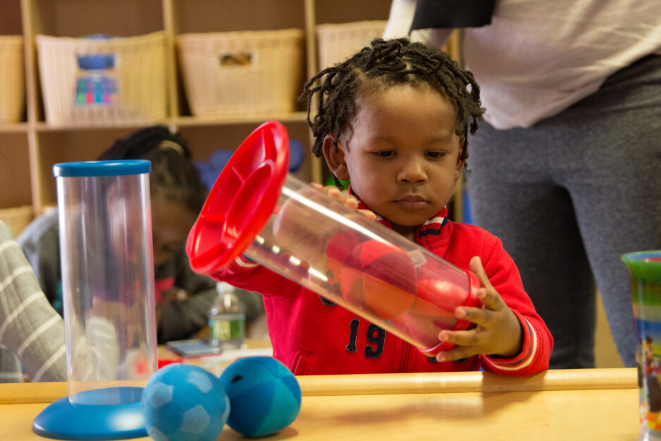 Three-Year-Old journey scholar wearing a red sweatshirt plays with a red ball.