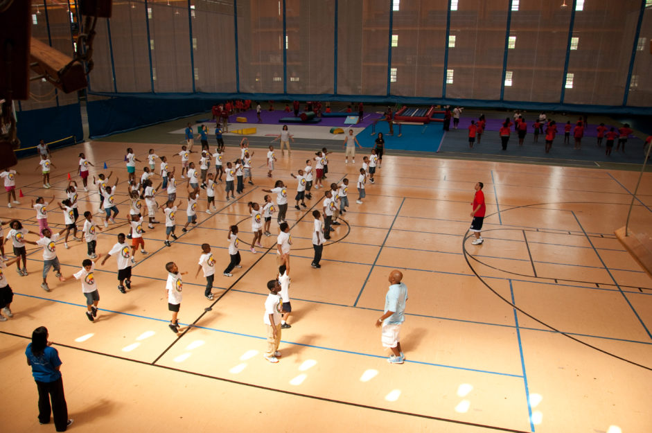 Community Members | With instructors guiding them, young kids participate in a fitness class in a large sports space.
