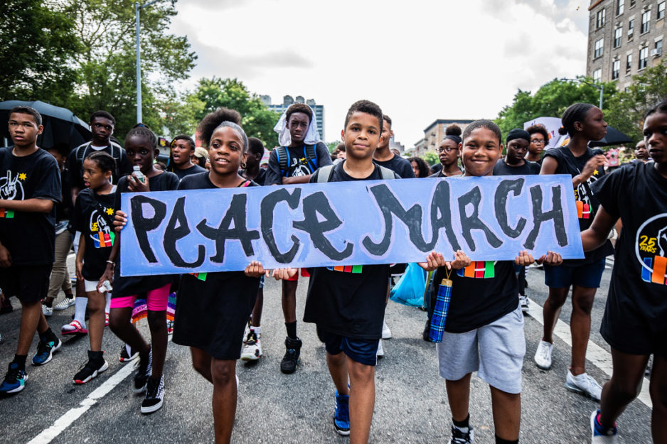 Three students, who are participating in a walk to promote peace, hold a sign that reads “Peace March.”