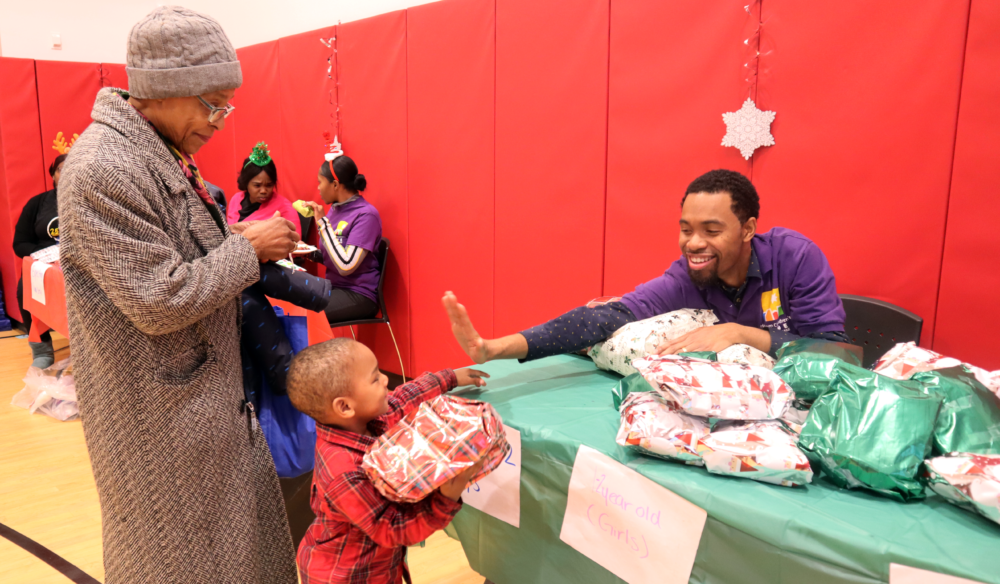 A young boy with his grandmother high-fives a man who handed him a gift at a holiday fair