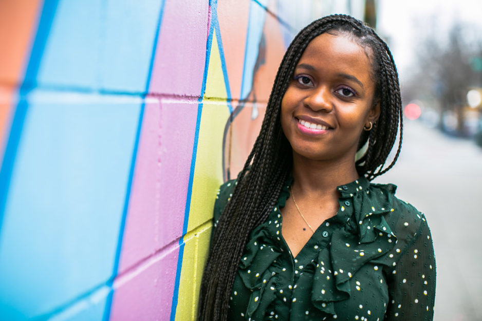 Harlem Children's Zone college coordinator Laressa Bordenave wears a green shirt poses against a colorfully painted mural