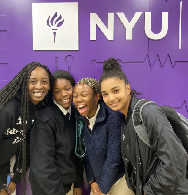 Four smiling teen girls stand in front of an NYU sign