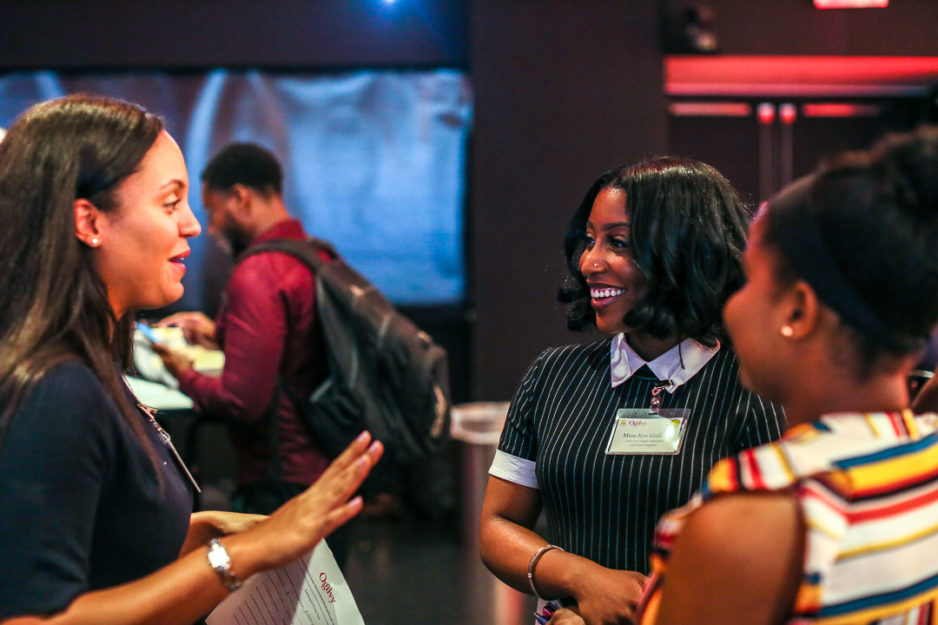 Two professional women discuss their work lives with a college student at a career networking event