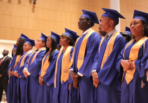 Youth Programs | High school graduates, in cap and gown, stand in a row at their graduation ceremony.