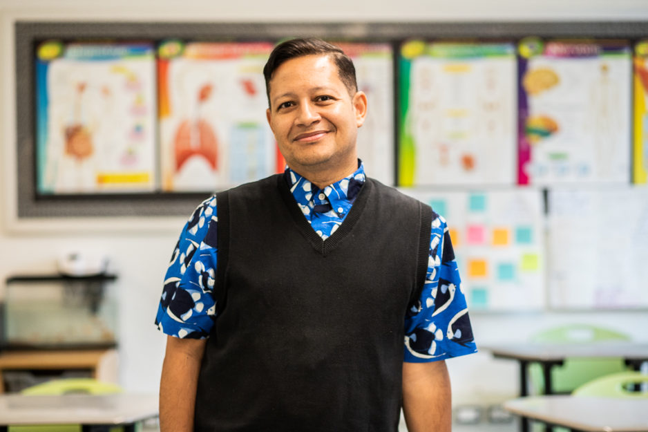 Harlem Children's Zone Promise Academy teacher Jerry Perez poses in a classroom and smiles.