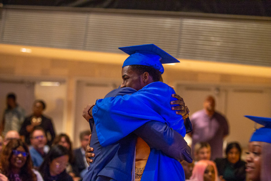 A young man graduate embraces an adult during the graduation ceremony.