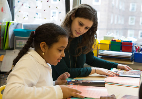 Career at HCZ |A teacher and a student look down at a book.
