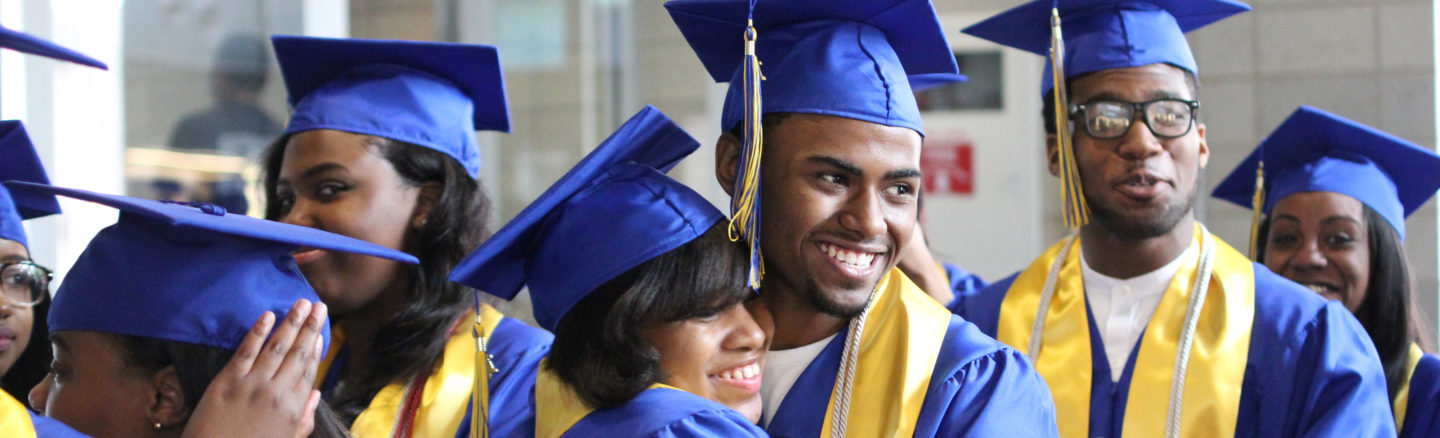 High school students in cap and gown smile and embrace at their graduation
