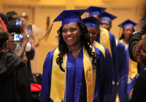 A Promise Academy High School graduate smiles and leads a line of her peers at graduation