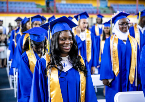 HCZ Promise Academy High School senior smiling in blue robe at graduation.