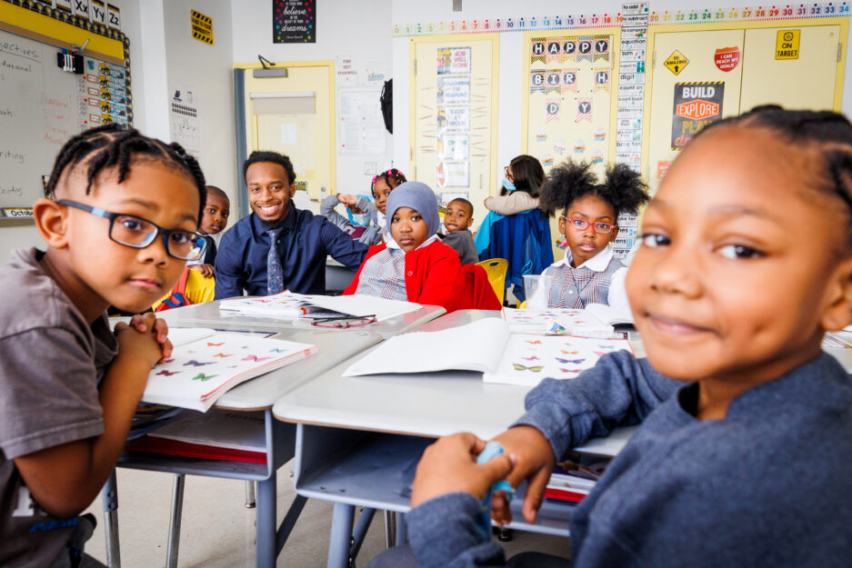 HCZ Promise Academy Elementary School teacher and scholars smile in a classroom.