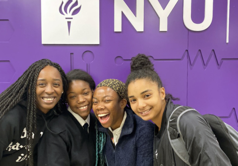 Scholars pose in front of purple New York University banner during a visit to the university.