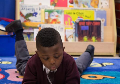 Young boy laying on carpet while reading