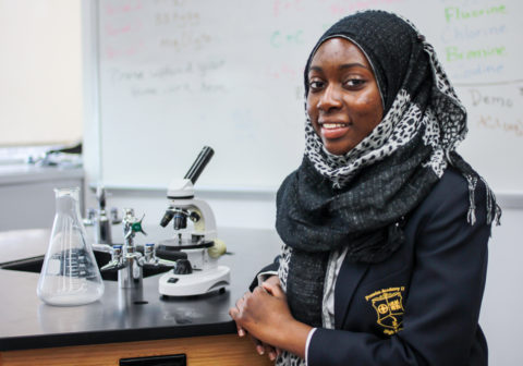 Promise Academy scholar next to microscope in classroom