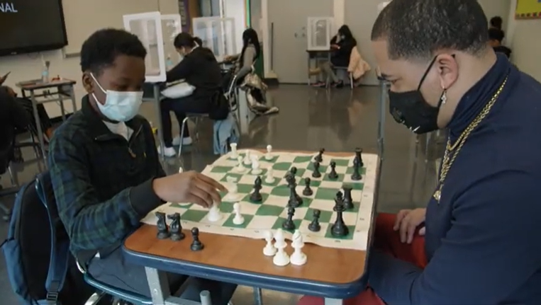 Student and teacher playing chess in classroom