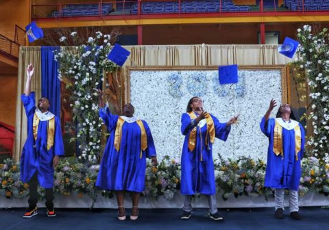 Students in blue robes throwing caps in air