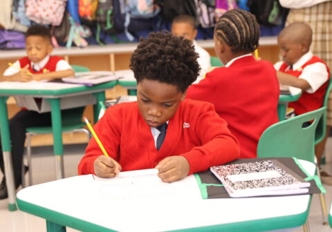 young male scholar sitting at his desk at school writing.