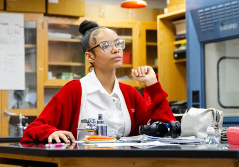 Female scholar sitting in a science lab focused on what is infront of her.