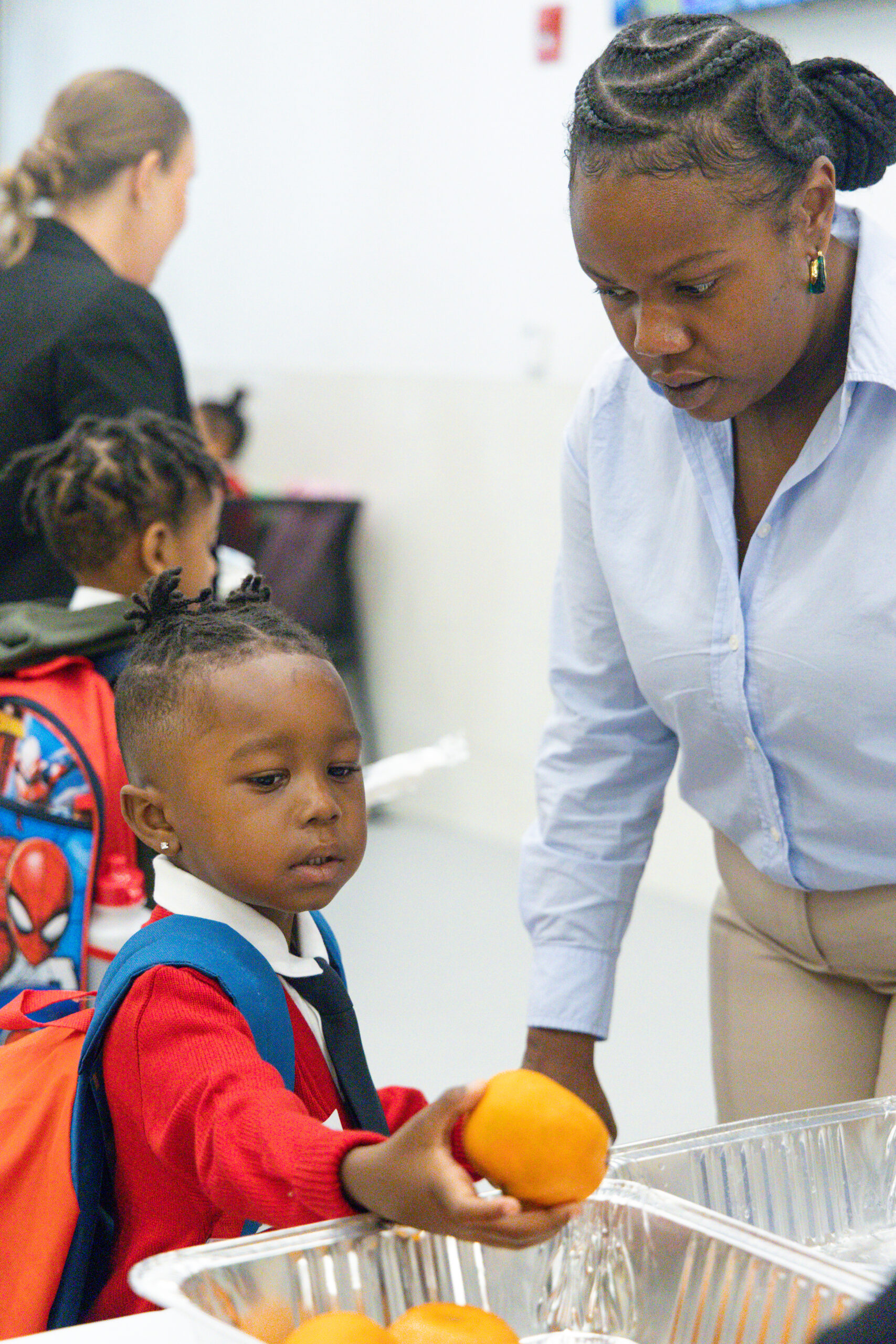 Young male scholar grabbing a fruit orange as a staff member watches him.