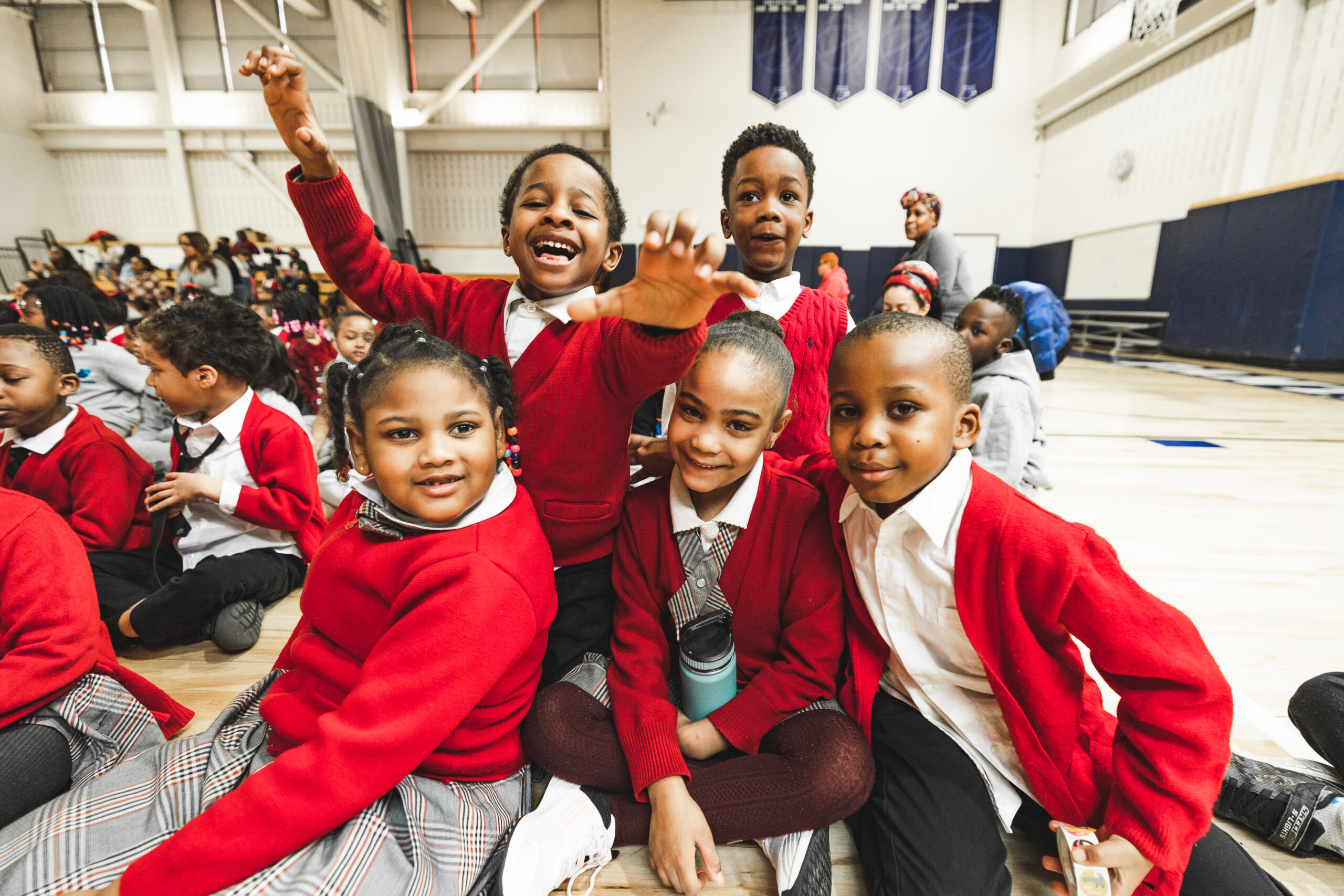 Five young scholars dressed in their red color uniforms happily engaging in a group photo.