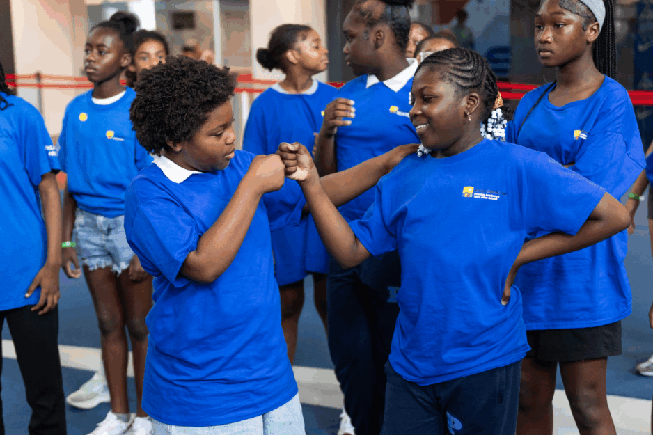 Two young scholars dressed in blue t-shirts celebrate with a fist-bump.