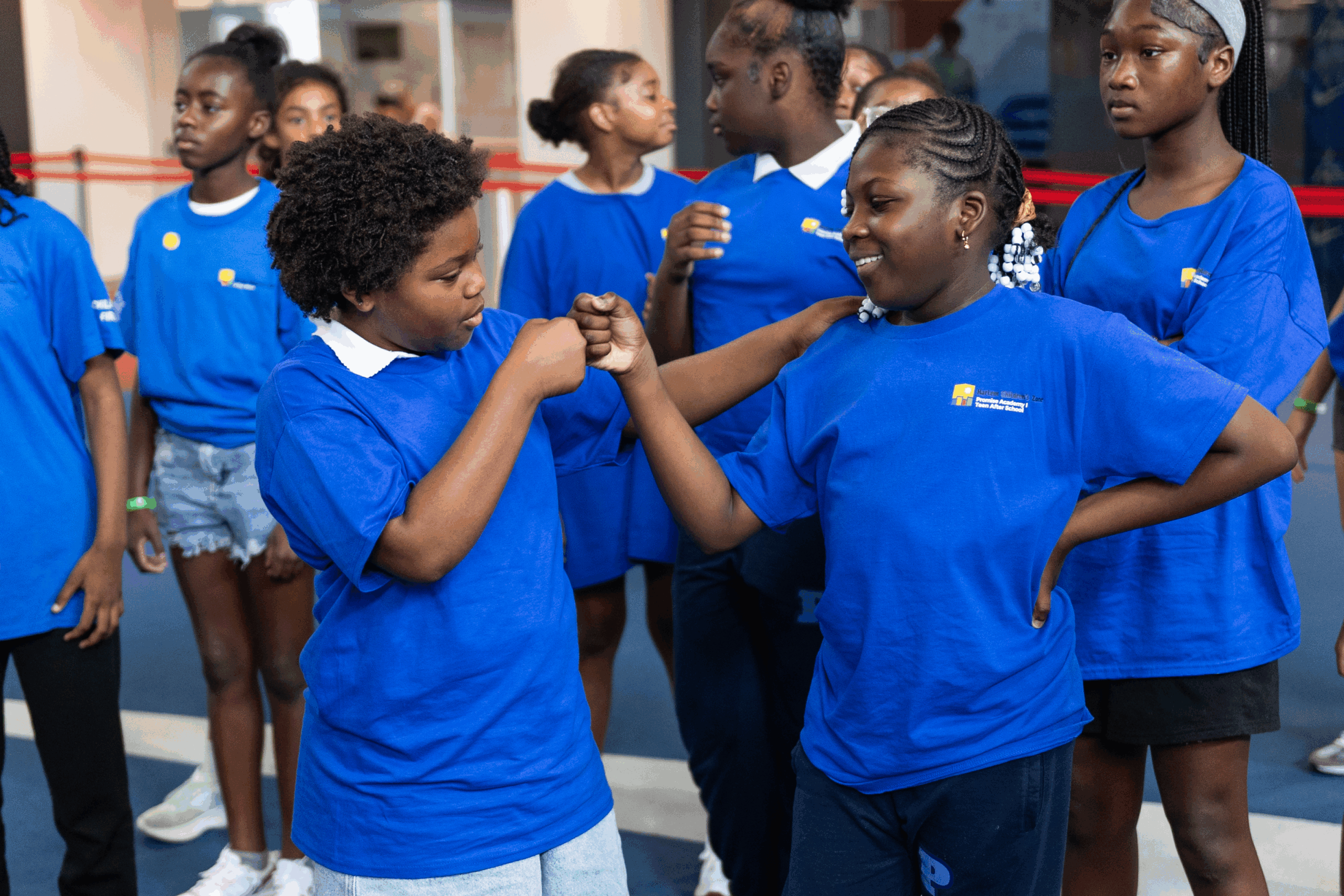 Two young scholars dressed in blue t-shirts celebrate with a fist-bump.