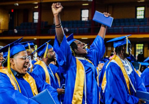 HCZ Promise Academy High School senior raises arms in celebration at graduation.