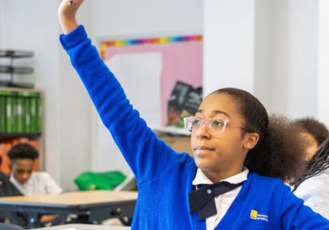 Scholar seated at their desk raising their hand.