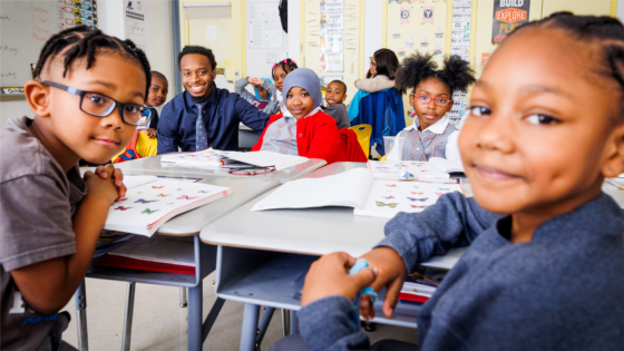 A group of students smile at the camera with their teacher in a classroom.