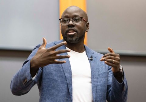 Man in grey suit and white t-shirt speaking.
