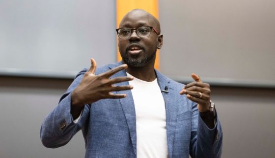 Man in grey suit and white t-shirt speaking.
